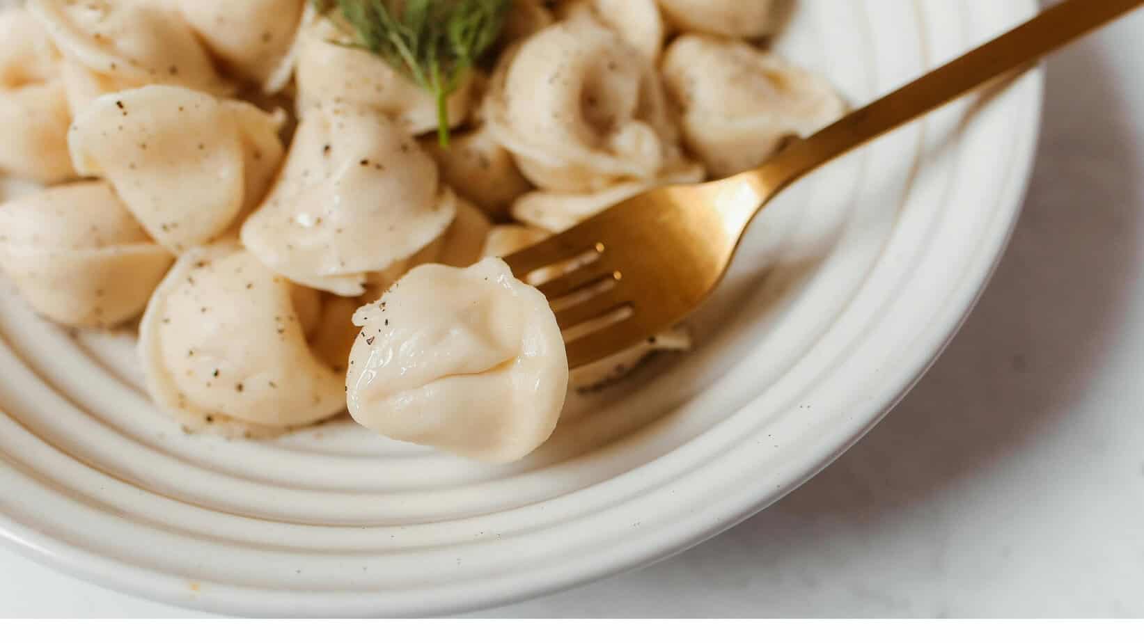 A close-up of a plate of dumplings, with one dumpling on a fork, showcasing a smooth, pale exterior. 