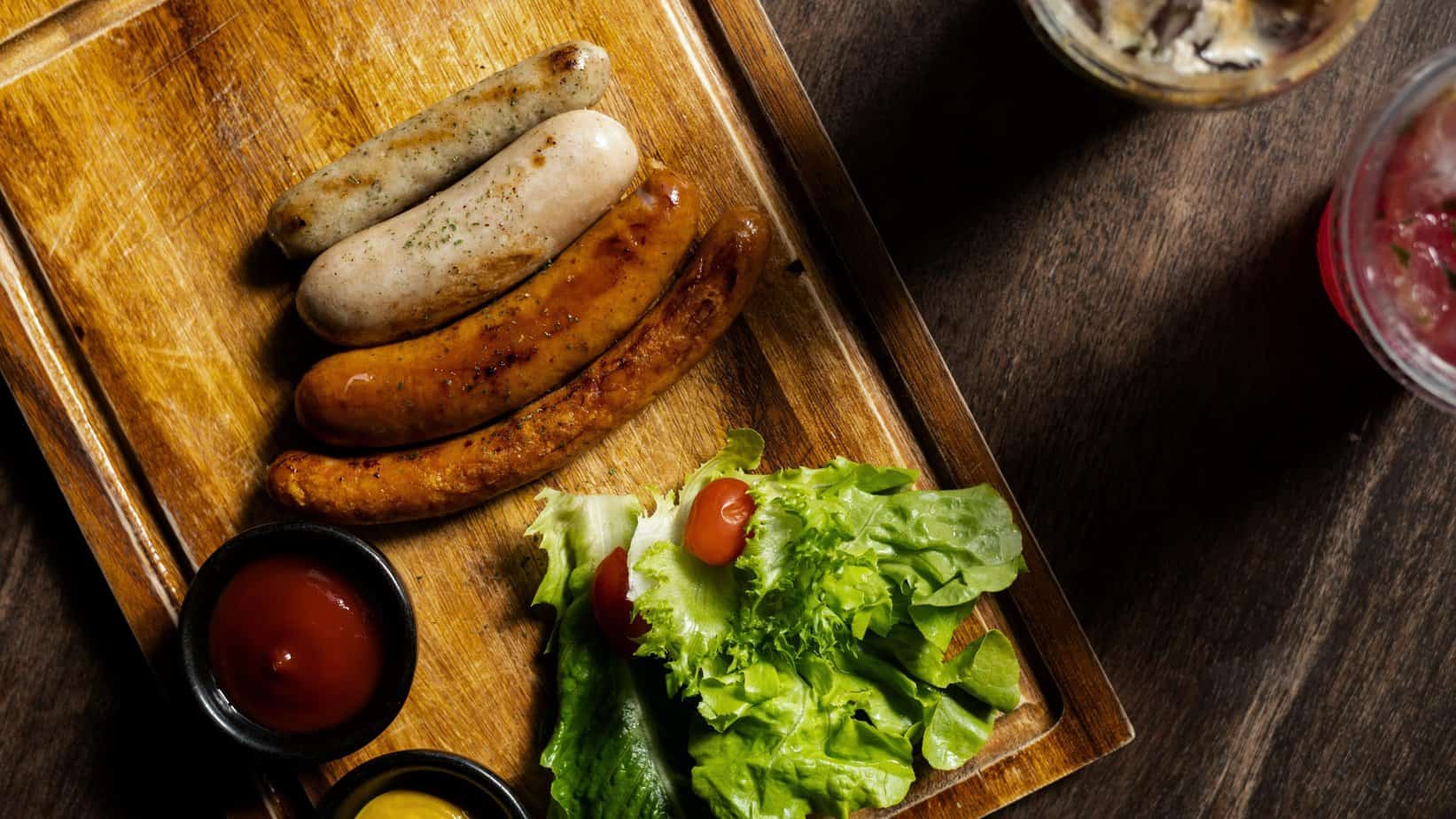 

Assortment of grilled chicken sausages and fresh lettuce salad on a wooden board, highlighting the savory components of a balanced meal.