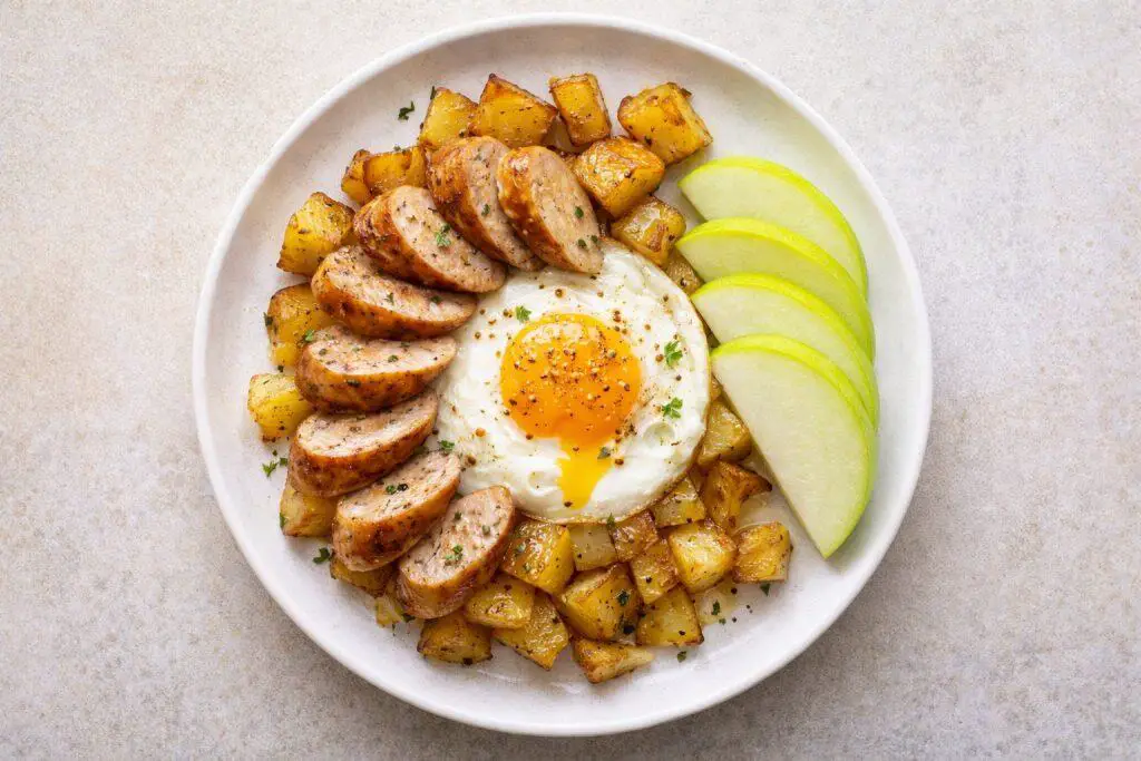 Plate with fried eggs, roasted potatoes, and fresh apple slices on a wooden background