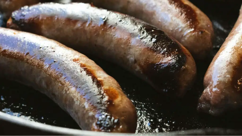 Juicy sausages browning in a cast iron skillet, showing how to Simmer Then Sear for Tender Sausage perfectly.