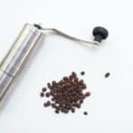 Brown coffee beans near gray stainless steel manual grinder