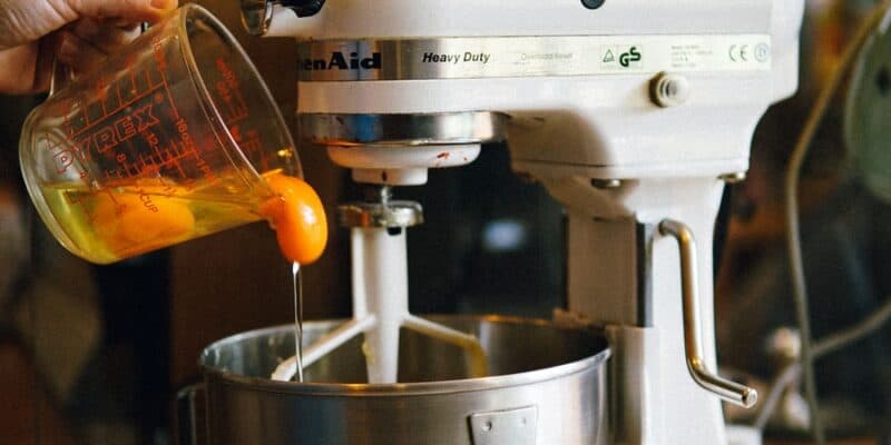 person pouring egg yolks on white stand mixer