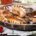 Savory meal components - Various grilled and roasted food items, including sausages, onions, and other vegetables, presented on a patterned plate with fresh greenery.