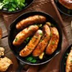 Savory sausage dish with dipping sauce - An arrangement of grilled sausages presented in a skillet, served with a side of red dipping sauce and various garnishes and seasonings.