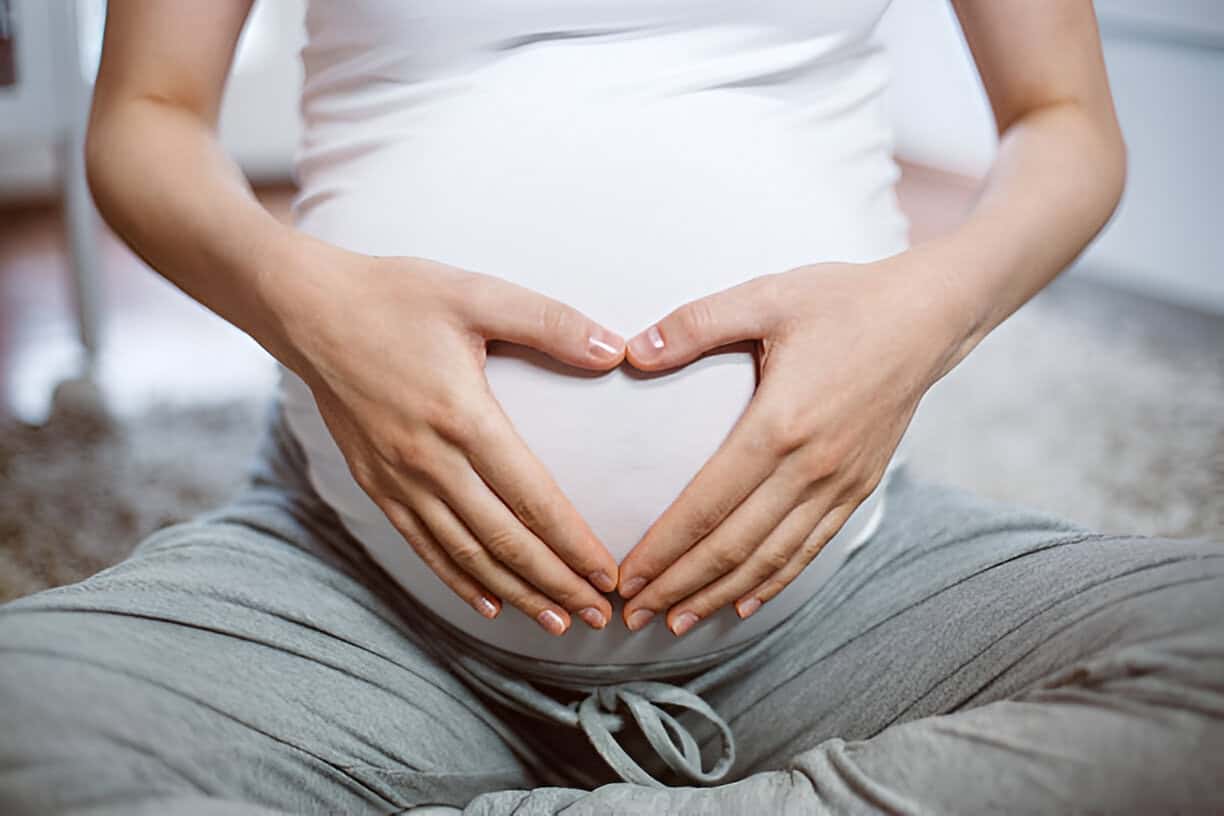 Pregnant woman forming a heart shape on her belly with her hands.