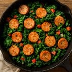 Top-view of a healthy chicken sausage and kale skillet dinner in a rustic cast iron pan on a wooden table, perfect for nutritious and easy low-fat meals.