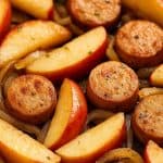 Chicken sausage and apple skillet with caramelized onions in a rustic pan, showcasing a hearty, healthy meal with sweet and savory flavors.