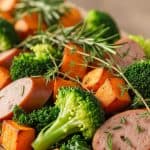 Sliced chicken sausage with roasted sweet potato cubes and fresh broccoli, garnished with herbs on a wooden board, healthy chicken sausage and sweet potato meal idea