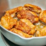 Close-up of crispy-skinned chicken thighs frying in a cast iron skillet.