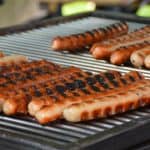 Close-up of a sizzling, juicy chicken sausage on a grill with a smoky, charred surface.