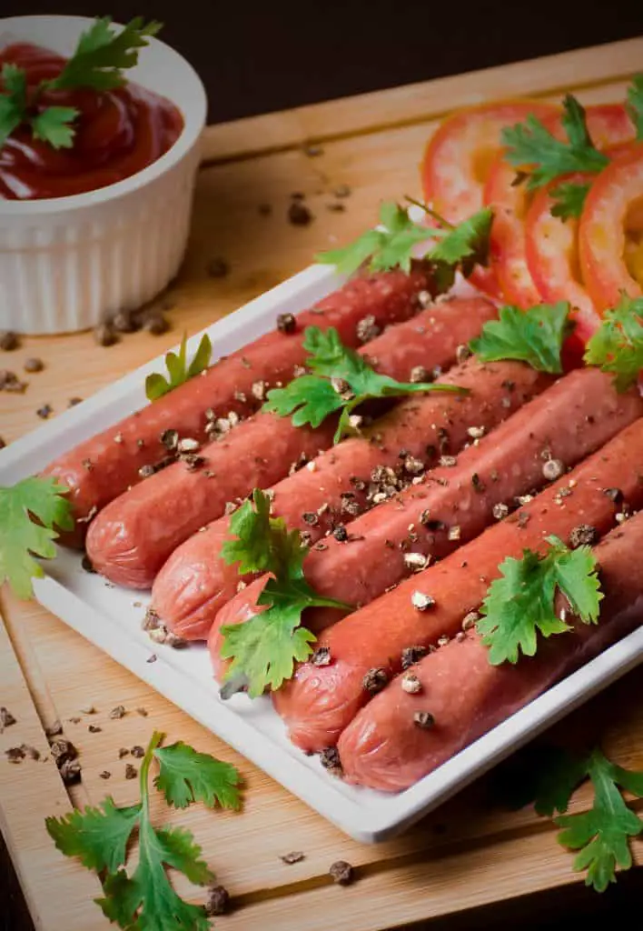 An assortment of savory, juicy sausages displayed on a wooden cutting board, accompanied by a side dish of condiment. 
