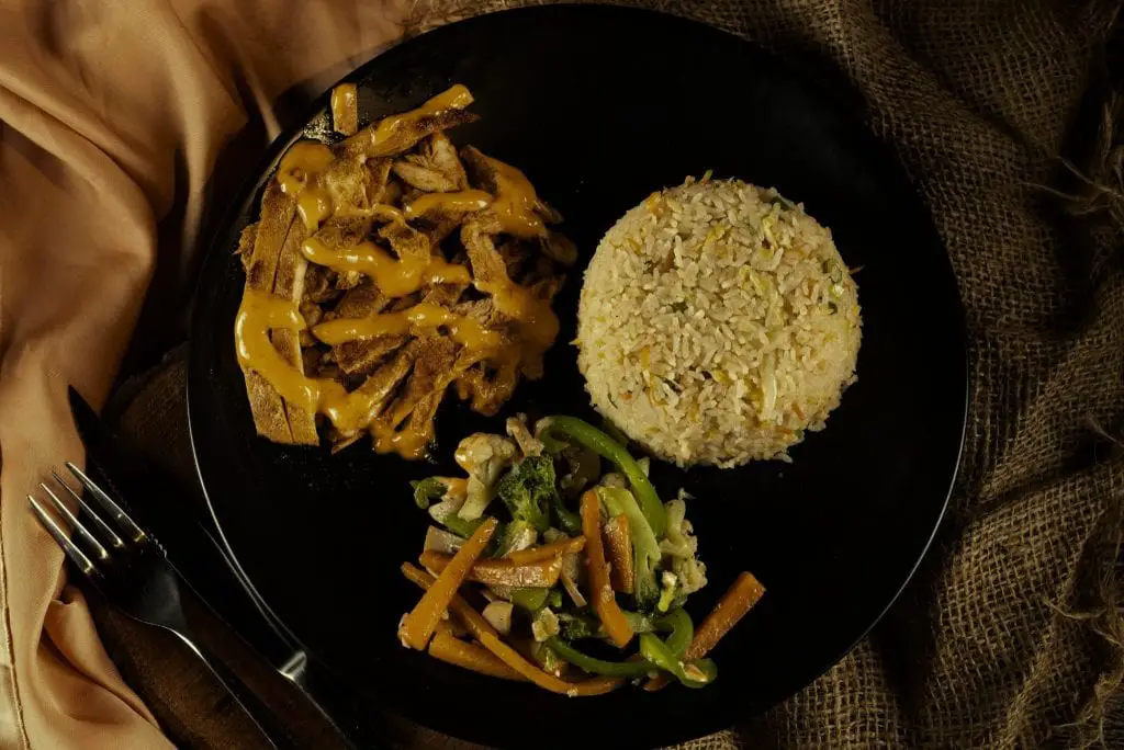 A meal with chicken sausage, cauliflower rice, and stir-fried vegetables on a black plate. Credits: pexels.com (Photo by Meraj Kazi)