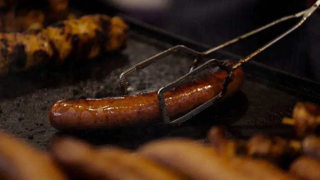 A large chicken sausage being grilled, with other sausages in the foreground, relevant to "do chicken sausages have carbs.