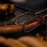 A large chicken sausage being grilled, with other sausages in the foreground, relevant to "do chicken sausages have carbs.