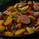 Close-up of a skillet filled with colorful chicken sausage and veggie stir fry, including peppers, onions, and potatoes.