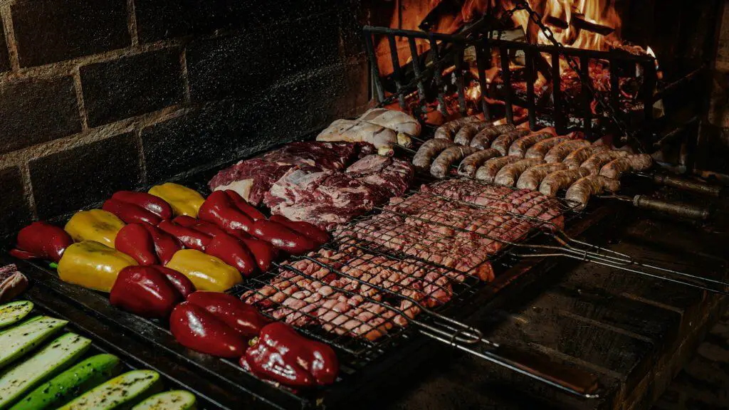 Assorted chicken sausage and other meats, alongside bell peppers and zucchini, grilling over an open fire.