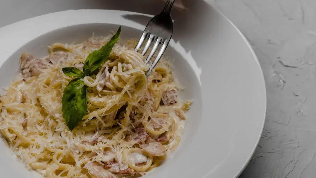 A fork lifts creamy chicken and sausage fettuccine alfredo with grated cheese from a white bowl.