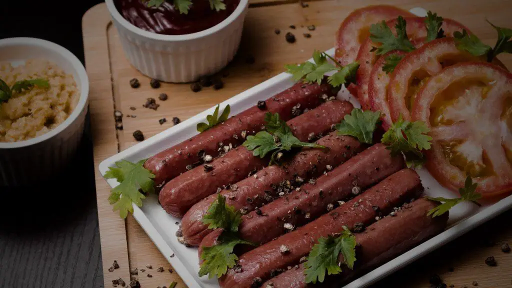 Cooked chicken sausage garnished with herbs and pepper, served with tomatoes and dips, showing chicken sausage meaning.