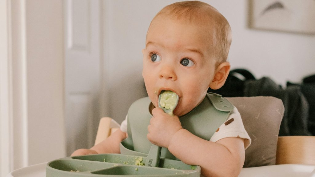 A baby enjoys a meal, exploring Chicken Sausage for Baby: Tasty & Safe First Food, in a high chair.