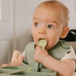 A baby enjoys a meal, exploring Chicken Sausage for Baby: Tasty & Safe First Food, in a high chair.