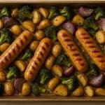 Roasted chicken sausages, potatoes, peppers, and herbs arranged on a sheet pan.