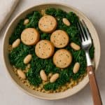 Chicken sausage with quinoa and kale, garnished with herbs, served in a ceramic bowl.
