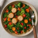 Grilled chicken sausage with quinoa, colorful veggies, herbs, served on a rustic wooden plate.