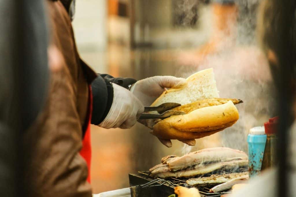 A person using tongs to place chicken sausage cut up into a bun, illustrating how to cook chicken sausage cut up.