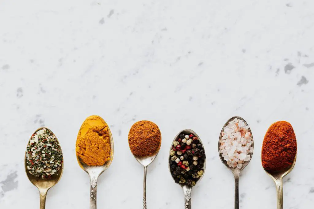 A variety of spices in spoons, ready to be used in a chicken sausage sheet pan recipe for added flavor.