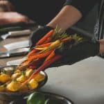 A chef holding colorful vegetables, preparing for a chicken sausage sheet pan recipe.
