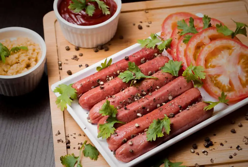 Grilled sausages and fresh vegetables on a wooden board, garnished with parsley and spices.