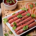 Grilled sausages and fresh vegetables on a wooden board, garnished with parsley and spices.