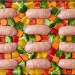 Sheet pan meal featuring chicken sausages nestled among roasted broccoli, bell peppers, and carrots.