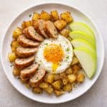 Plate with fried eggs, roasted potatoes, and fresh apple slices on a wooden background