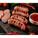 Grilled sausages on a slate board with dipping sauce and chili peppers, perfect result of how to cook chicken sausage from frozen