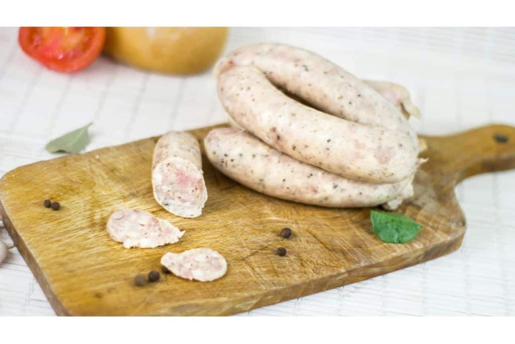Raw chicken sausage links sliced on a wooden board with herbs and peppercorns — Is Chicken Sausage Low-Fat compared to pork?