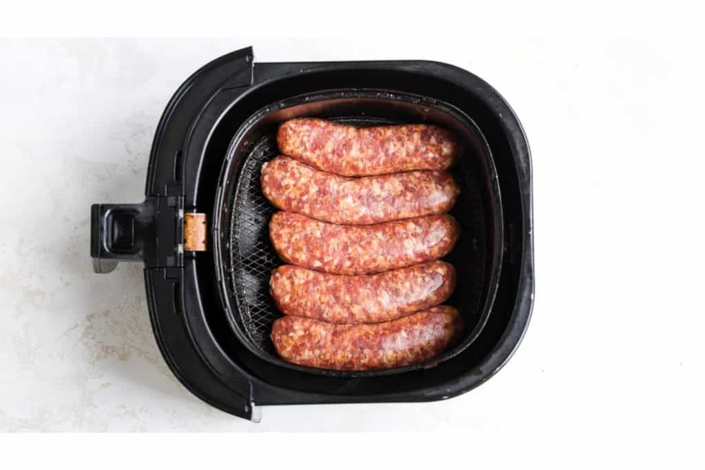 Raw sausages placed in a black air fryer basket, exploring Cooking Method: Does Grilling or Air Frying Reduce Fat content?