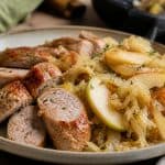 Chicken sausage with sauerkraut served with apples and onions on a rustic plate in a warm kitchen setting.